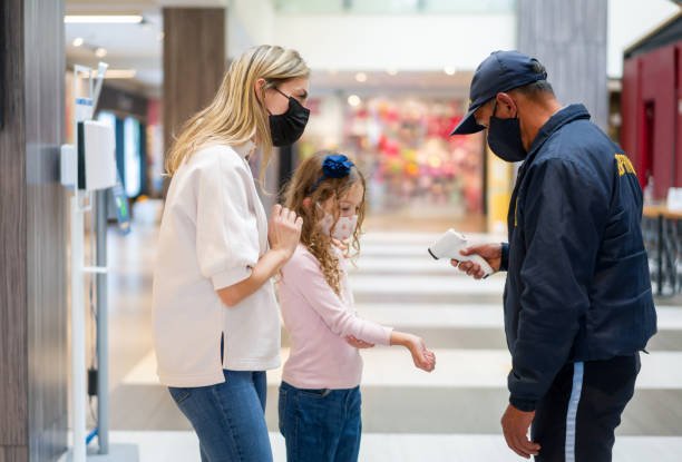 Mother and daughter at a temperature checkpoint while shopping at the mall and wearing facemasks - COVID-19 pandemic lifestyle concepts