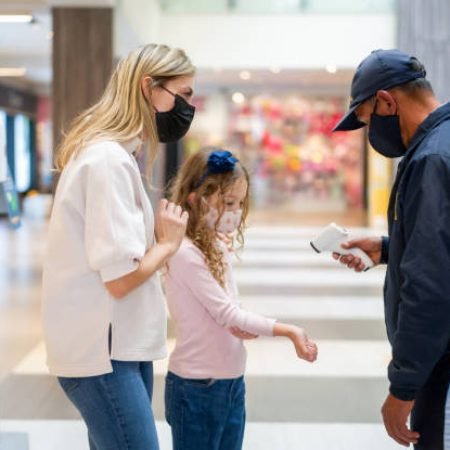 Mother and daughter at a temperature checkpoint while shopping at the mall and wearing facemasks - COVID-19 pandemic lifestyle concepts